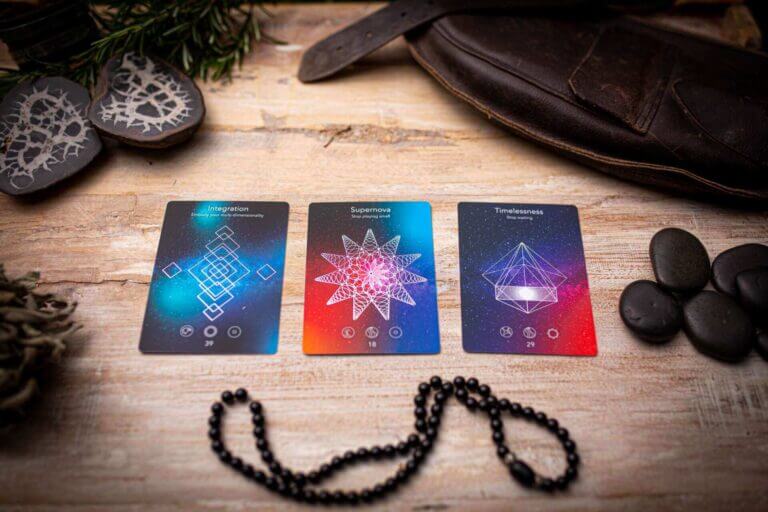 Three tarot cards featuring integration, supernova, and timelessness designs, with black beads and stones in the background.