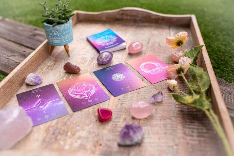 A collection of spiritual healing cards displayed with crystals and flowers on a wooden tray, featuring vibrant colors and mystical designs.