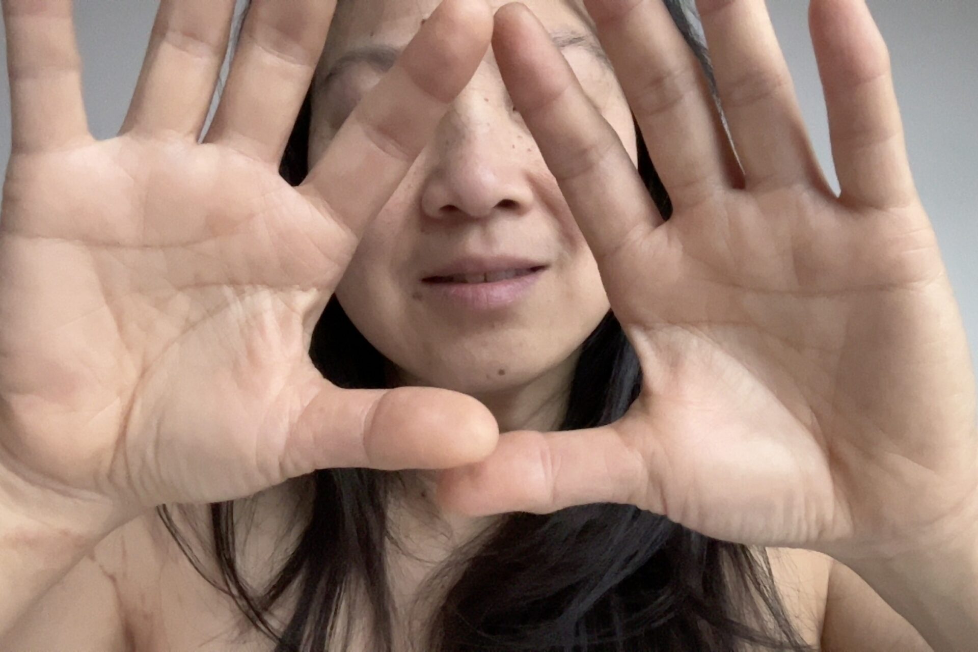A woman framing her face with hands, showcasing a natural expression and skin tone, emphasizing a connection with self and mindfulness.