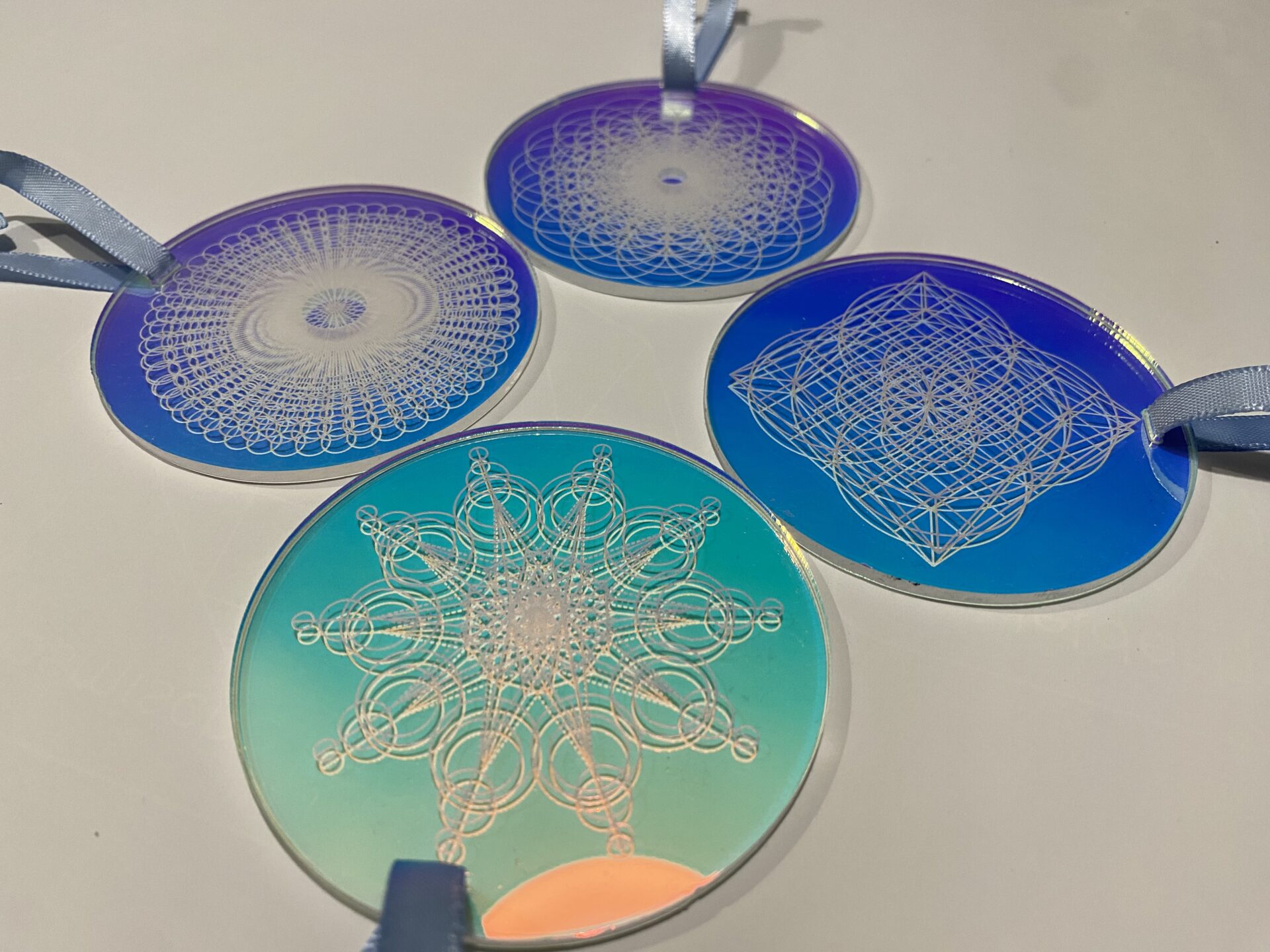 Four decorative acrylic ornaments featuring intricate geometric designs and vibrant blue gradients, ideal for home decor or gifts.
